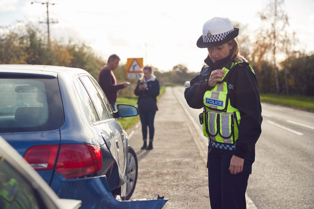A police officer uses a radio to call in details about a car wreck at the accident scene while a driver wonders if you can claim a car accident without a police report.