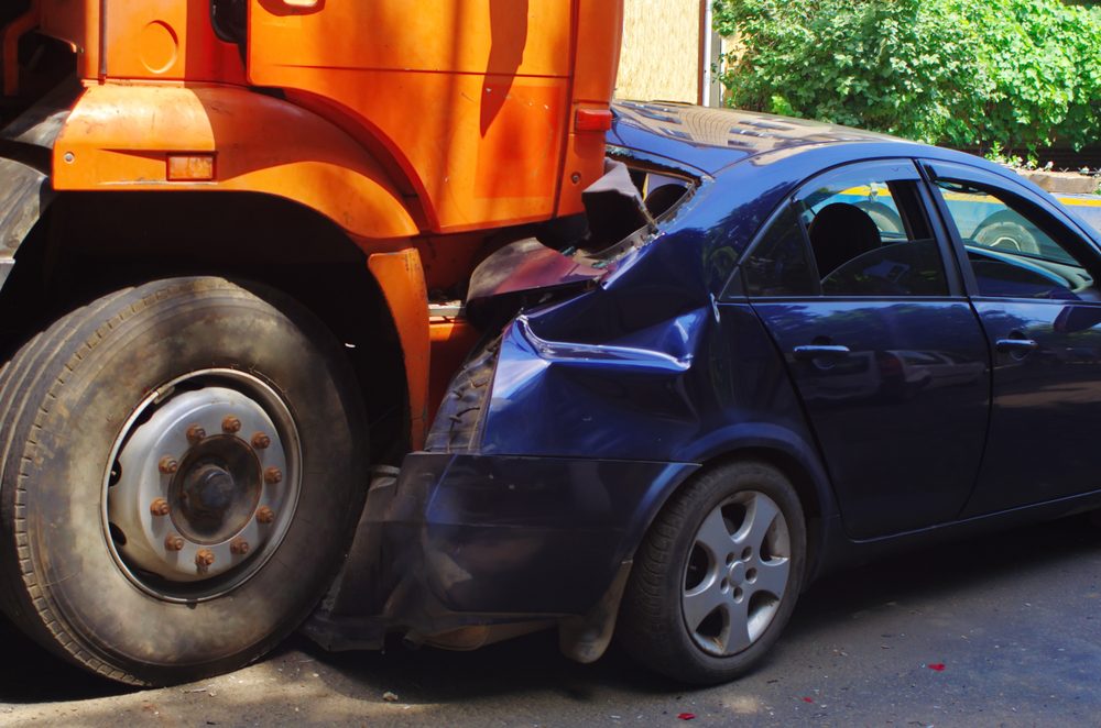 Un automóvil de pasajeros azul es aplastado bajo un camión, mientras en algún lugar el conductor del vehículo se pregunta quién es responsable en un accidente de camión.