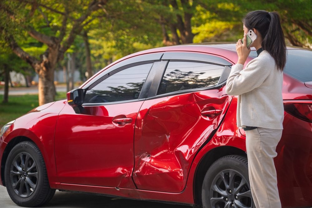 A woman on the phone next to a damaged car. What to do after a car accident that’s not your fault in WA.